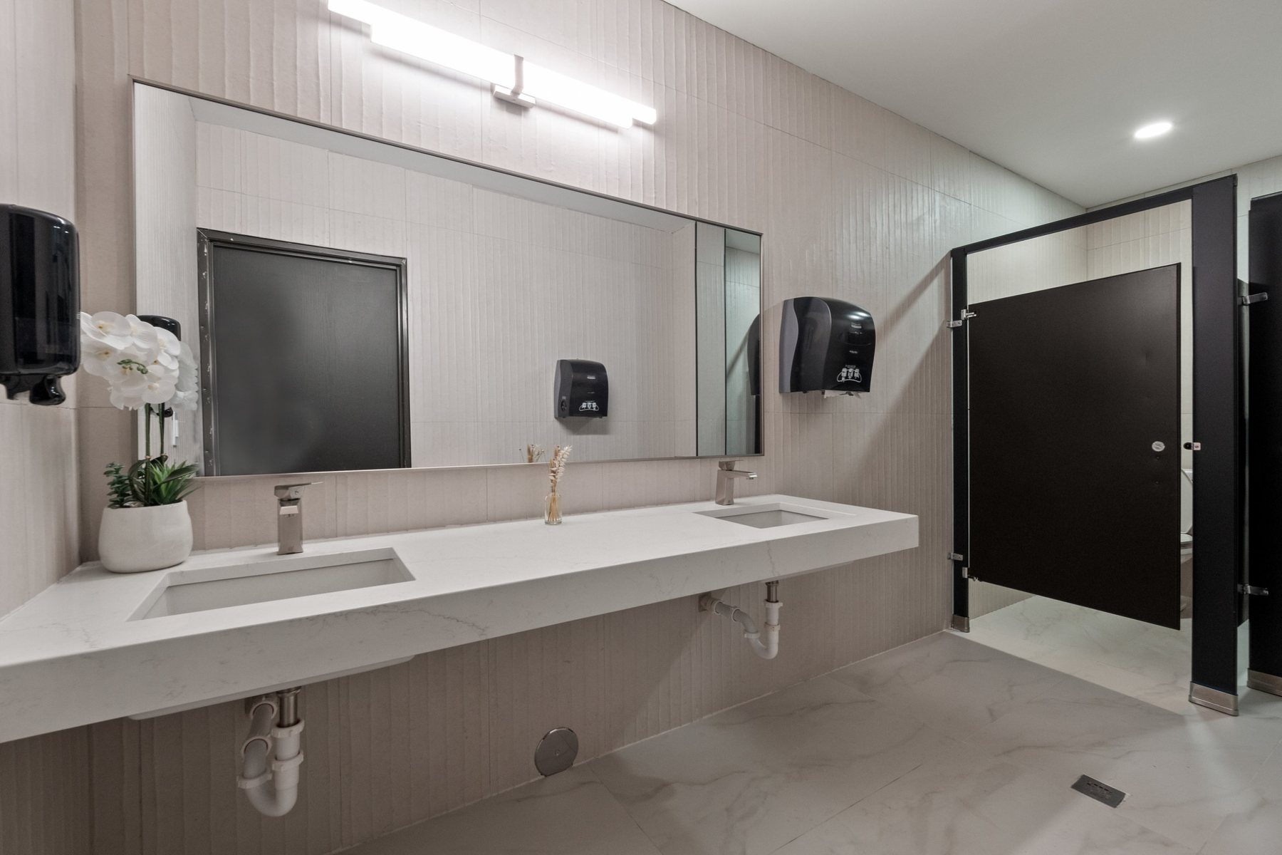 Renovated women's room in the private office area with quartz double vanity and marble-look tile