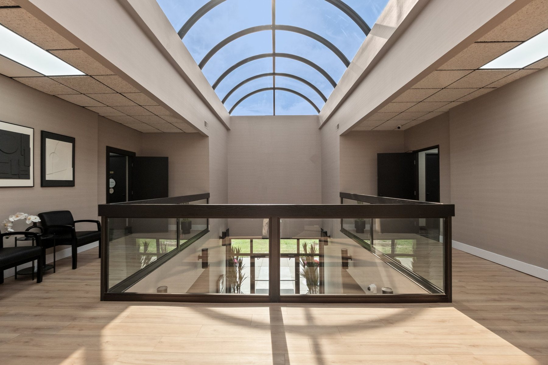 Second-floor lobby under the arched glass skylight, with waiting area and glass railing overlooking the first floor